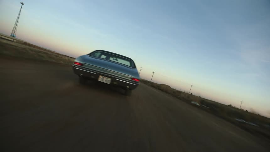 The blue car is speeding on the dirt road