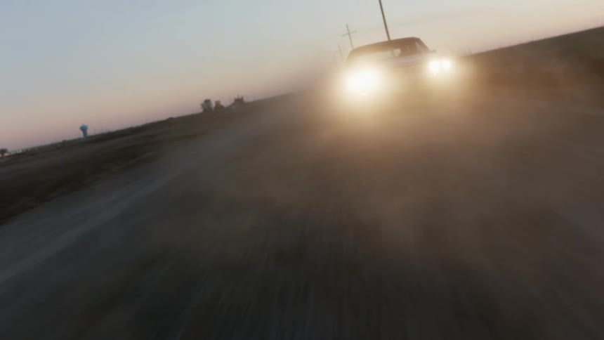 A view of a car driving down a dirt road
