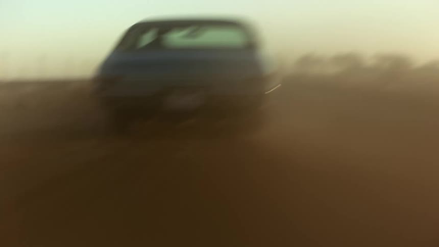 Car speeds along dirt road kicking up dust