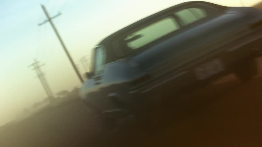 A car driving on a road next to a grassy field with the sky and clouds in the background