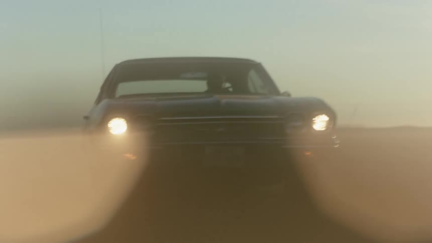 A view of a car driving down a dirt road at dusk