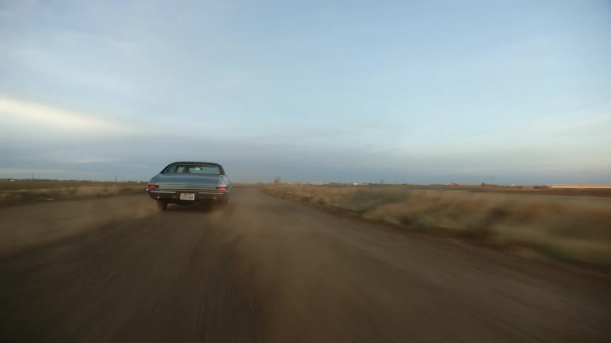 Car speeds along road through countryside kicking up dust