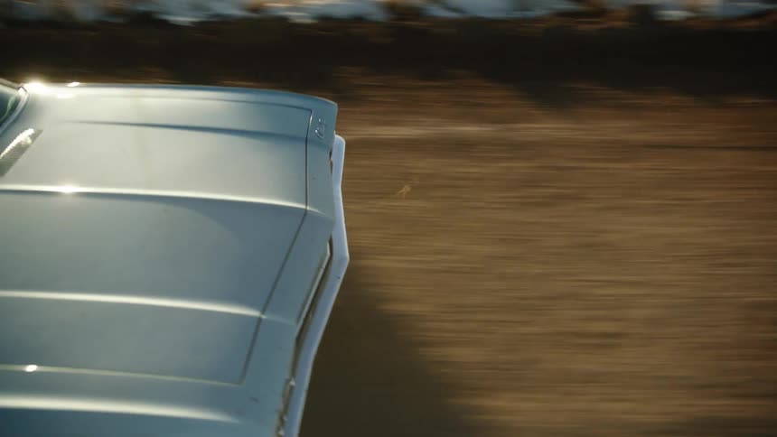 A car driving on a road next to a grassy field with the sky and clouds in the background