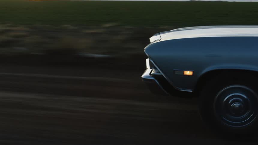 An antique car traveling on a rural road at sunset