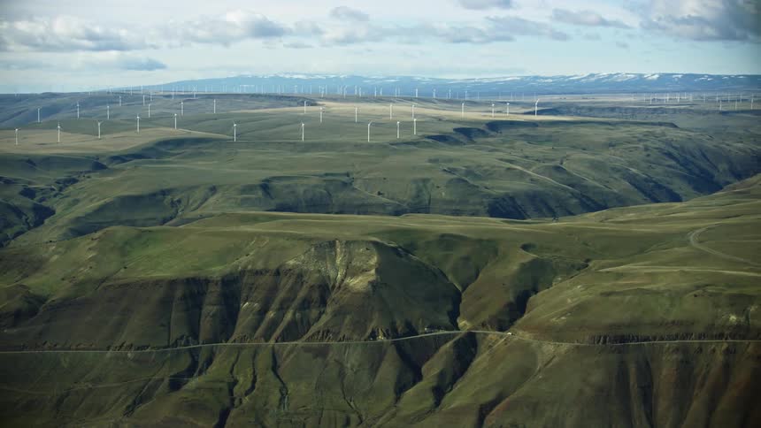 Aerial shot of a vast and expansive canyon with wind turbines spinning on the horizon generating wind energy from a renewable source