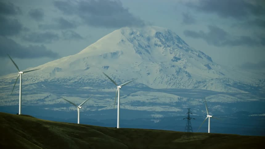 Aerial shot flying by wind turbine after wind turbine with a massive mountain (Mount Adams) in the background in this high energy shot