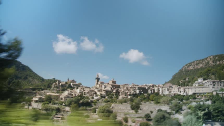 Town occupies terraced hill between two forested mountains under slightly cloudy sky
