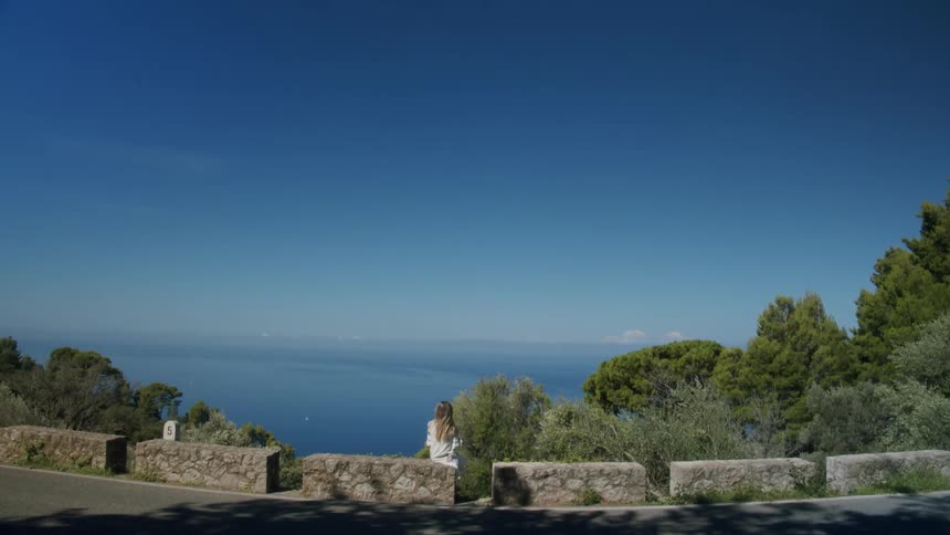 A view of a woman sitting on a wall at the beach
