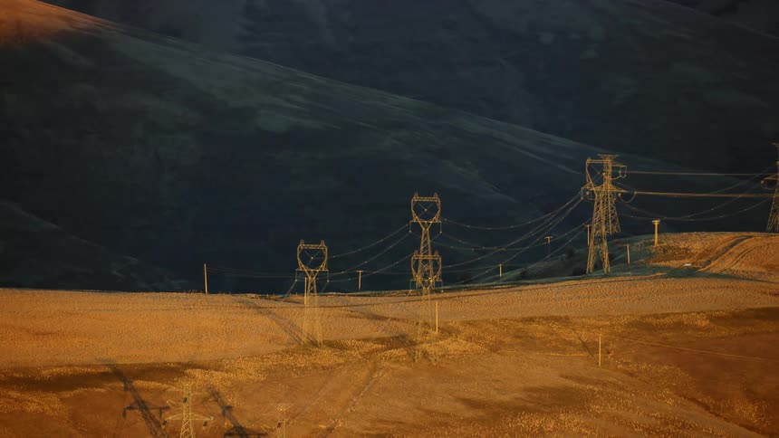 Electrical transmission lines moving energy on top of a large ridge at night as the sun is setting over golden hills