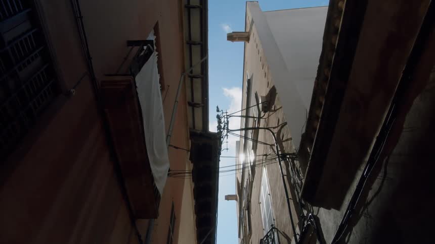 Clouds pass above narrow alley with fabric flapping on balcony
