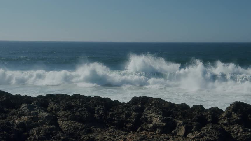Waves crash onto large boulders along the shore of the ocean