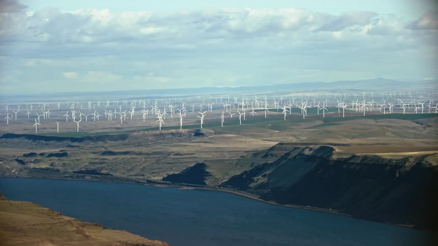 Stunning aerial of a large windfarm perched high above an expansive river corridor as the camera pans left to reveal the scene