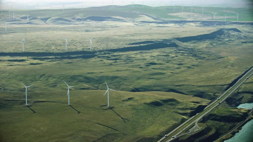 High altitude aerial shot showing a vast landscape full of wind turbines and a large river with a highway running nearby