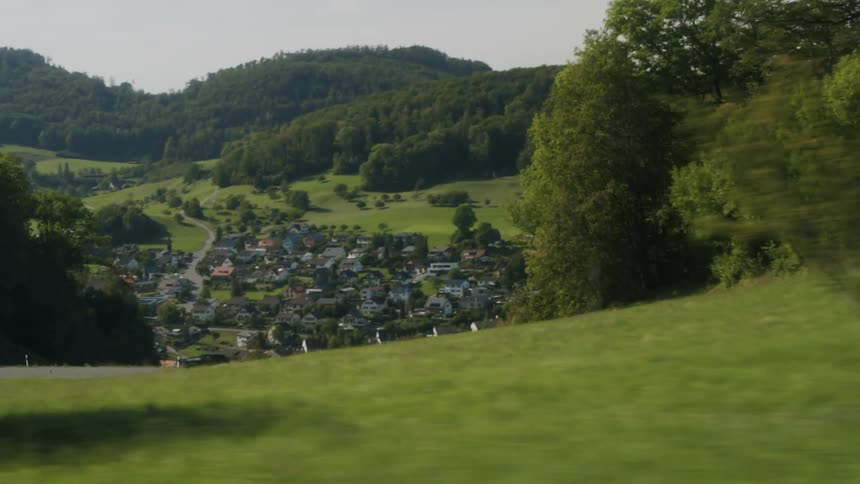 A car drives on a street above a neighborhood surrounded by hills