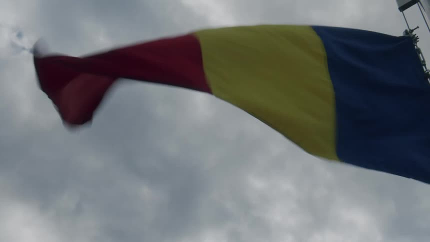 Romanian flag on a flagpole waving in the wind on an overcast day