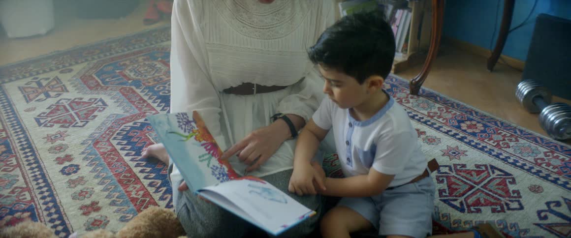 Mother and son reading a story book sitting on a carpet in a room at home