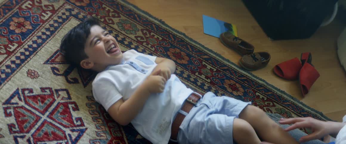 A woman tickles a boy lying on a rug