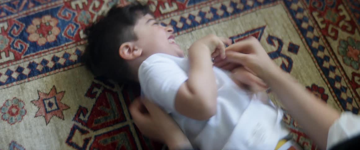 A mother tickles her son as he lies on a rug at home and laughs