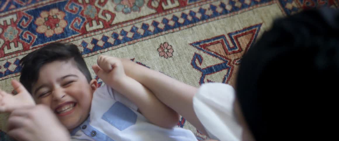 Person tickles young boy laying on a rug making him laugh and roll away