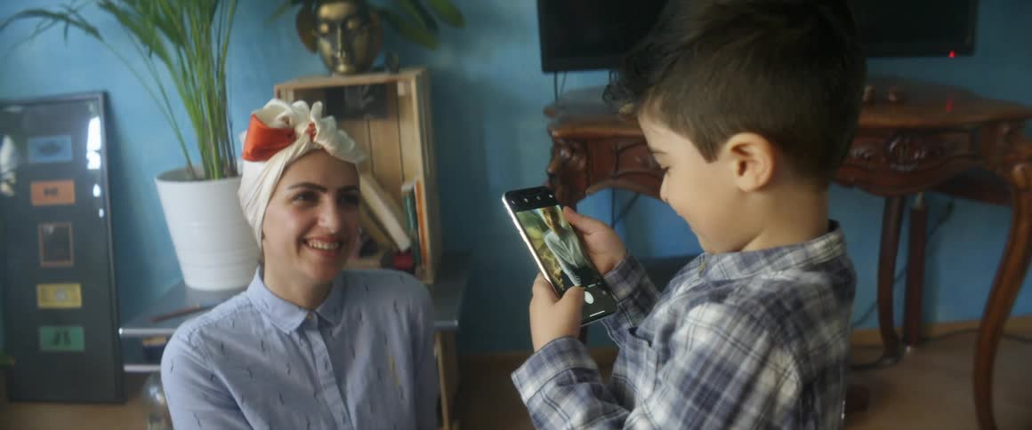 A young boy holds a cell phone and takes a photo of his mother