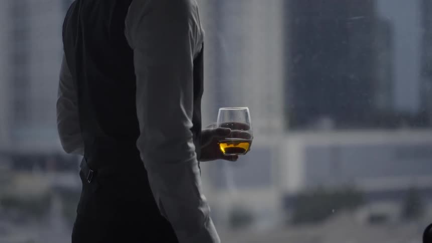 A man standing near a large window holding a drink