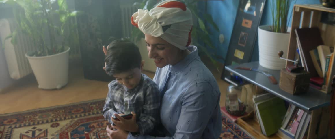 A boy sitting in his mothers lap takes a selfie of the two of them before showing it to the camera