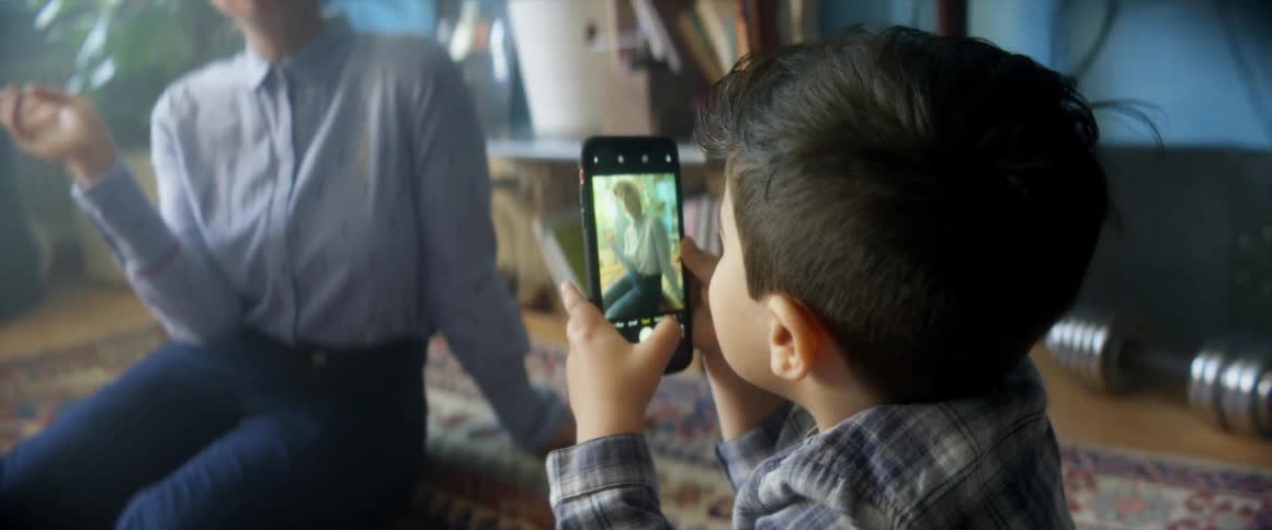 Son is taking a picture of his mother with a cell phone while sitting on the floor at home