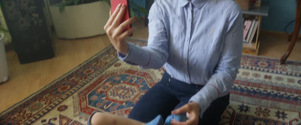 A woman with a smart phone playing with a boy in a room on the floor with plants in the background