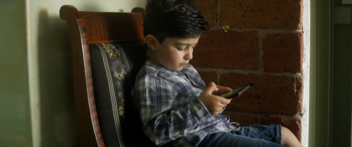 Small boy sitting in a chair in the corner of a room at home uses a smart phone