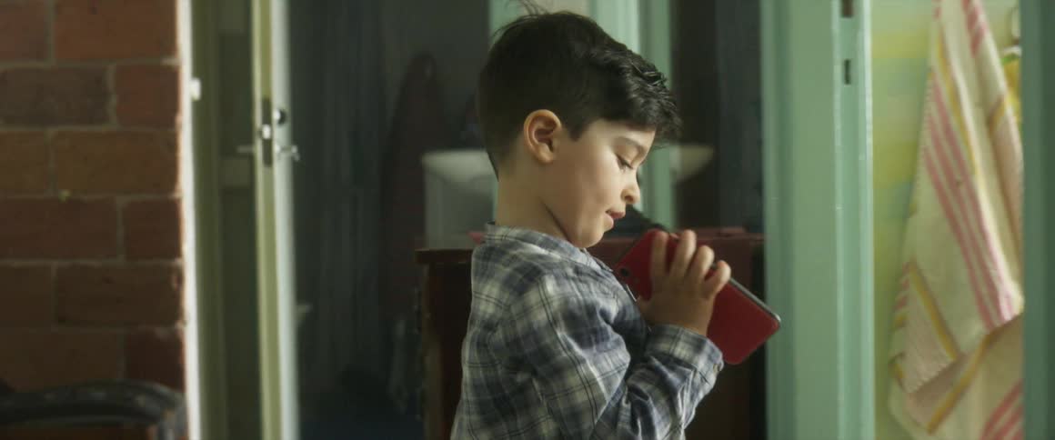 A boy fiddles with a smartphone while talking to someone out of frame
