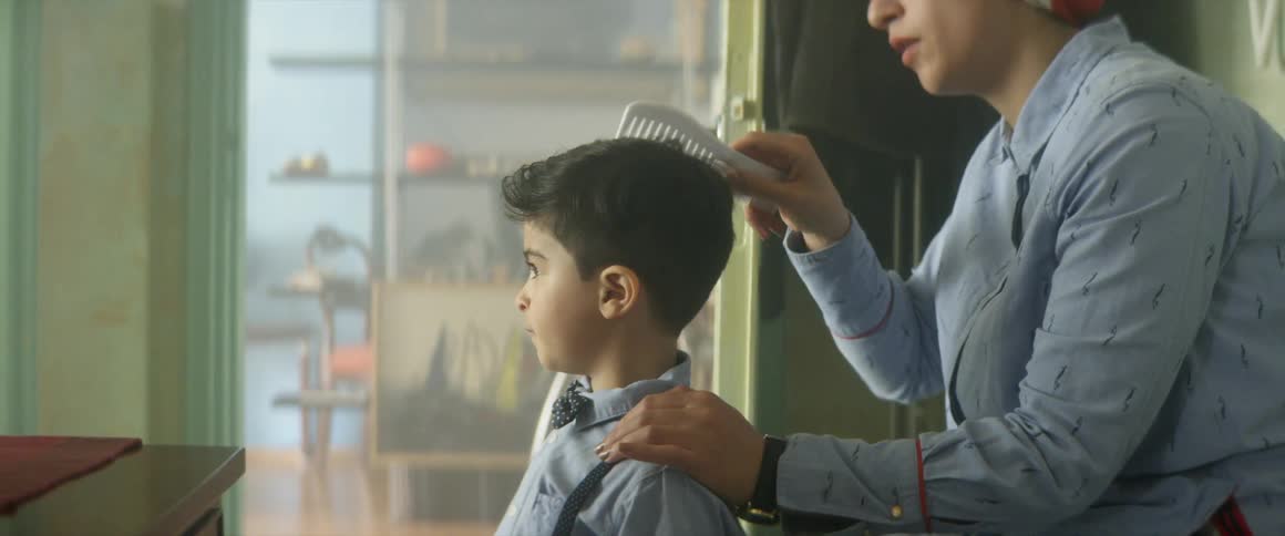 A woman combs her young sons hair while sitting indoors in a house during the day