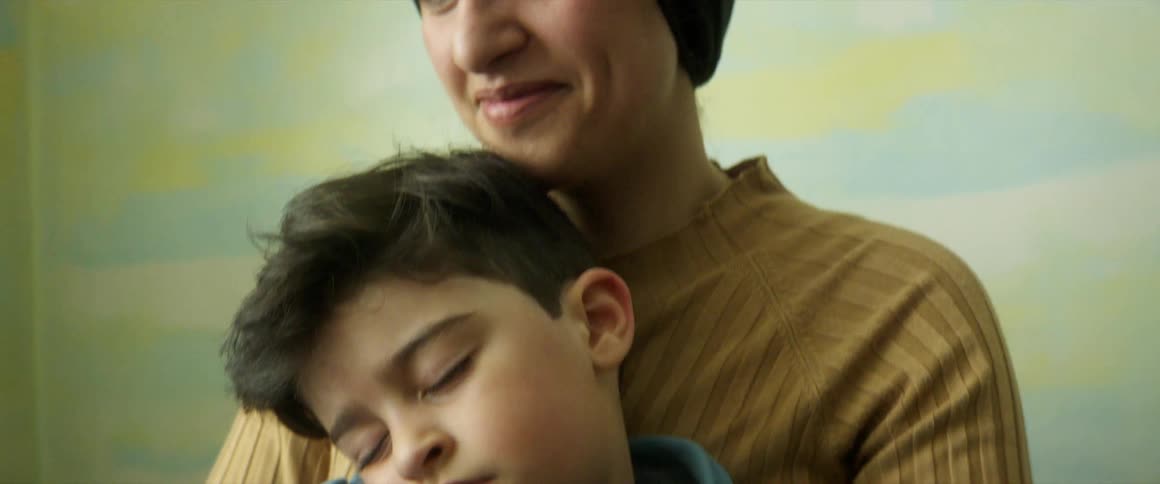 Smiling mother holds sleeping son while sitting at wooden table