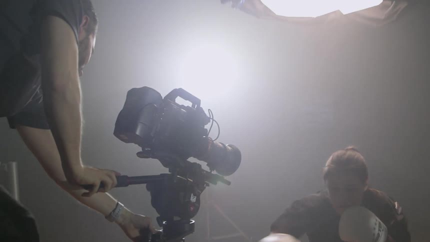 A camera man adjusts his camera as a woman spars under a large light