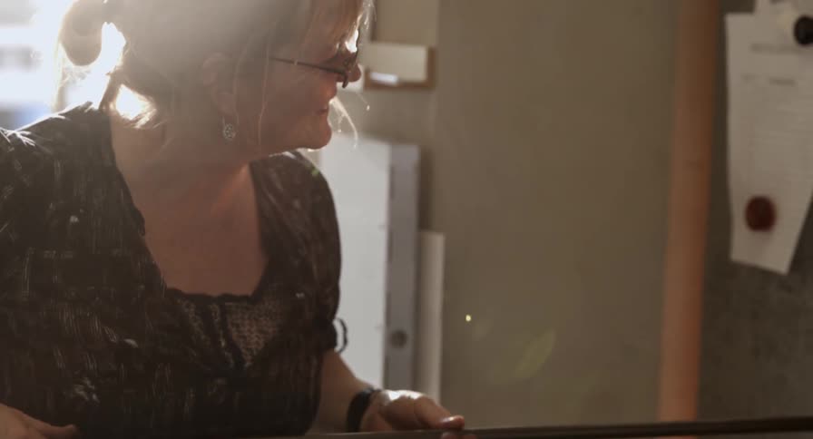 A female glassblower twists a thin pole around