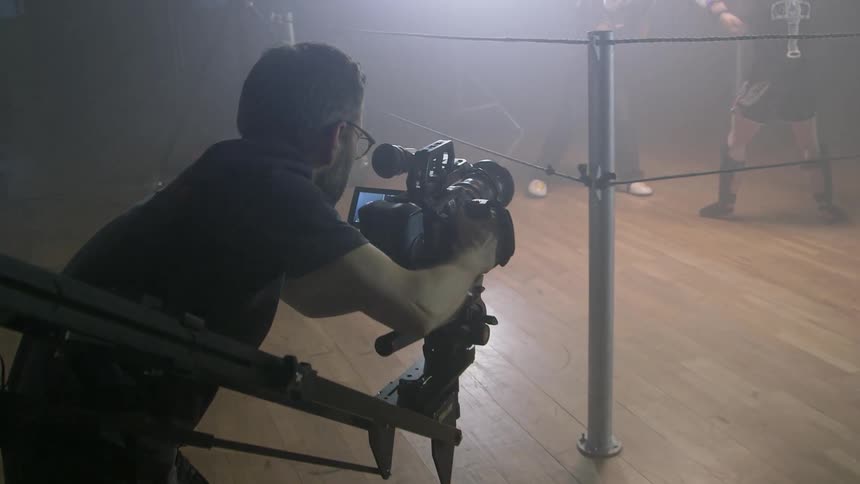 A cameraman films two boxers in a small ring