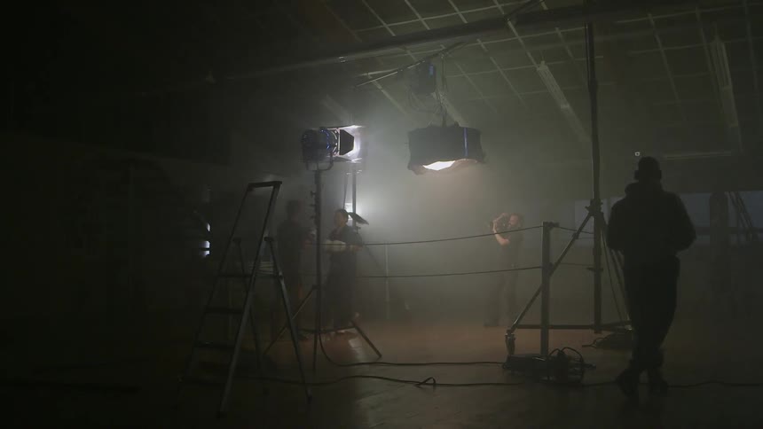 Two people kick each other in a boxing ring while several people record it