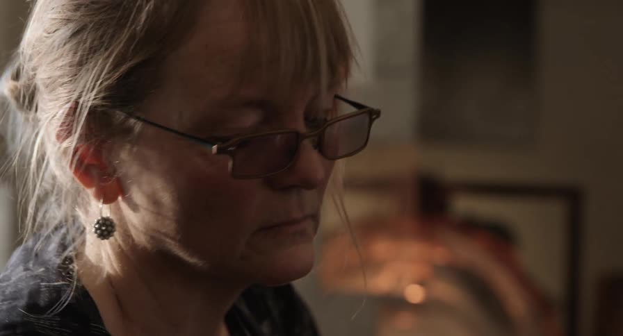 A woman wearing glasses looks down while concentrating