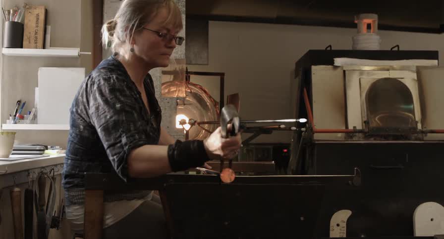 A woman is forming glass in a shop