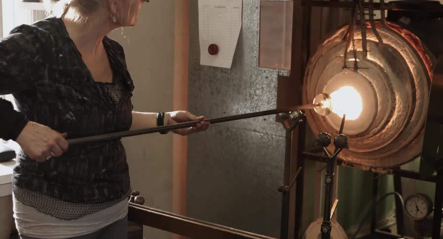 A woman is blowing glass in an oven