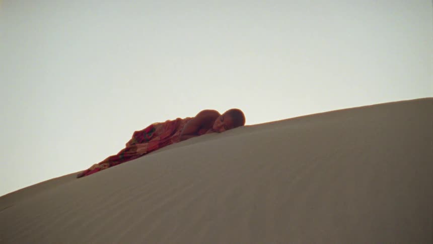 A woman resting on top of a sand dune in the desert at sunset