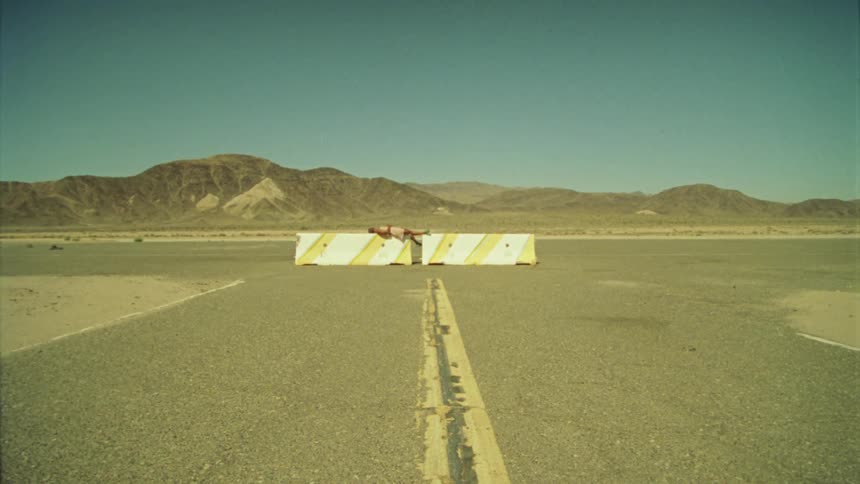 A woman resting over concrete barriers on a road in the desert close to the mountains