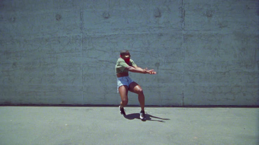 Young bald woman wearing a red bandana on her face energetically dancing in front a concrete wall