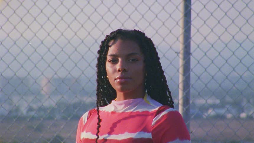 A teenager stands in front of a fence and looks ahead