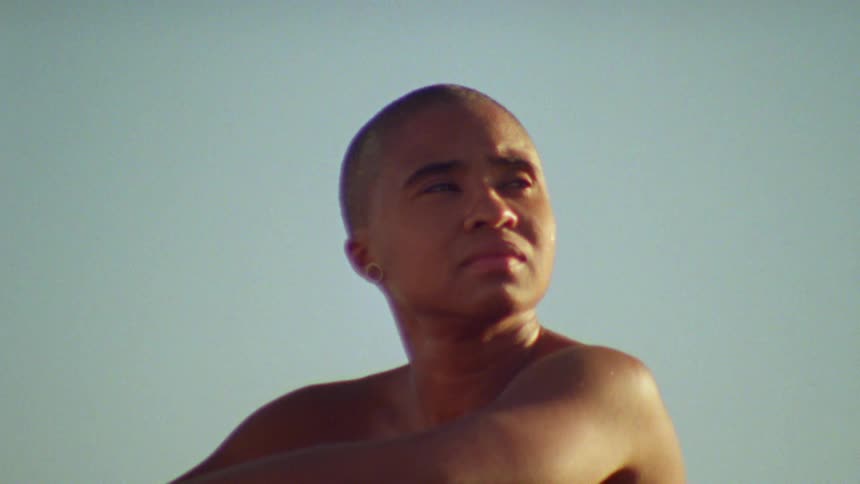Bald woman sitting in a sand dune in the desert looking at the horizon at sunset