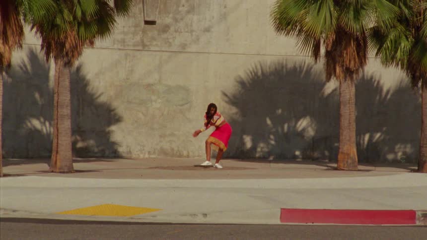Woman dances on sidewalk between palm trees near street