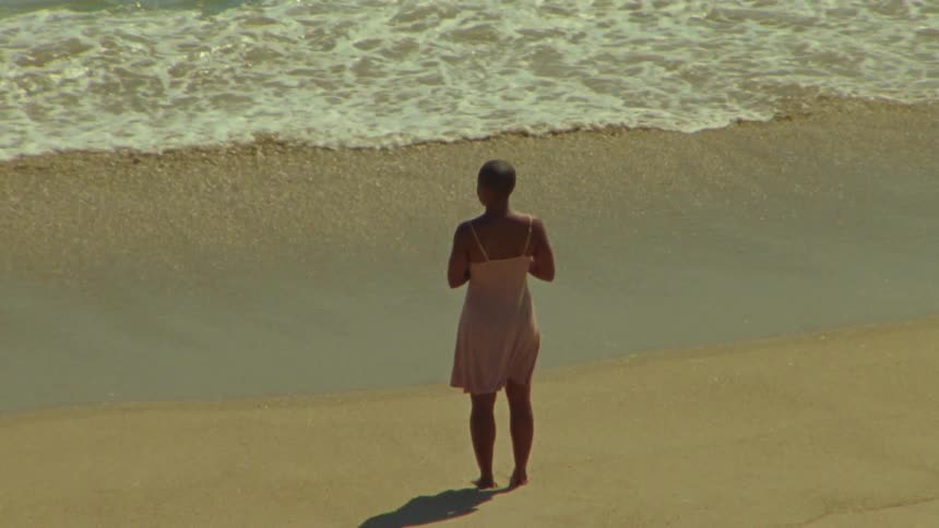 Woman wearing short dress stands on beach looking out to sea
