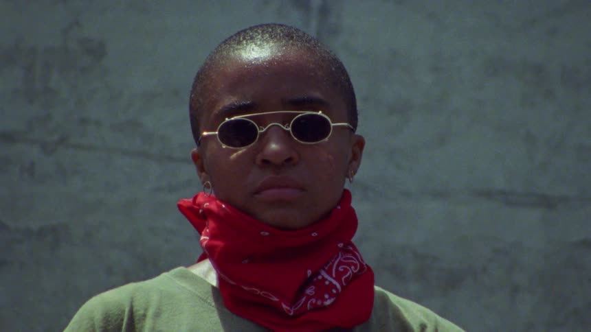 A woman wearing sunglasses pulls down her bandanna
