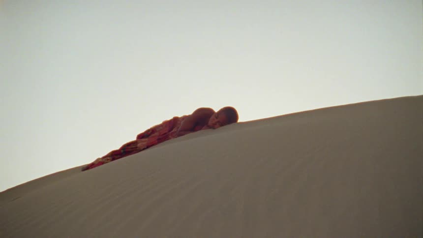 A young woman sleeps in the sand atop a sand dune in the desert during the day