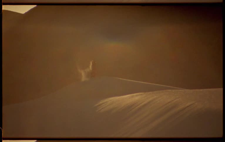 Sand runs through a persons hands and blows in the wind as they stand on a dune in the desert