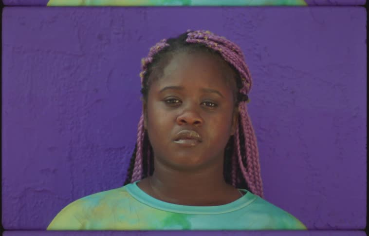 Woman standing against purple background with pale mauve hair extensions blinks